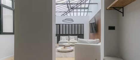 Un interior moderno con techo alto, una zona de estar central con sofá y mesa de centro, y un tragaluz.
