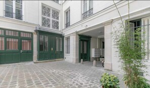A courtyard with a cobblestone floor, green doors, and a white building with multiple windows. - Stunning Apartment  - 4BR/8P - Gare de l'Est (Paris)