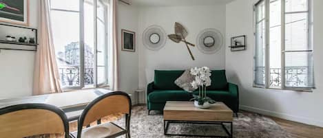 A living room with a green sofa, a coffee table, and a dining area with chairs.