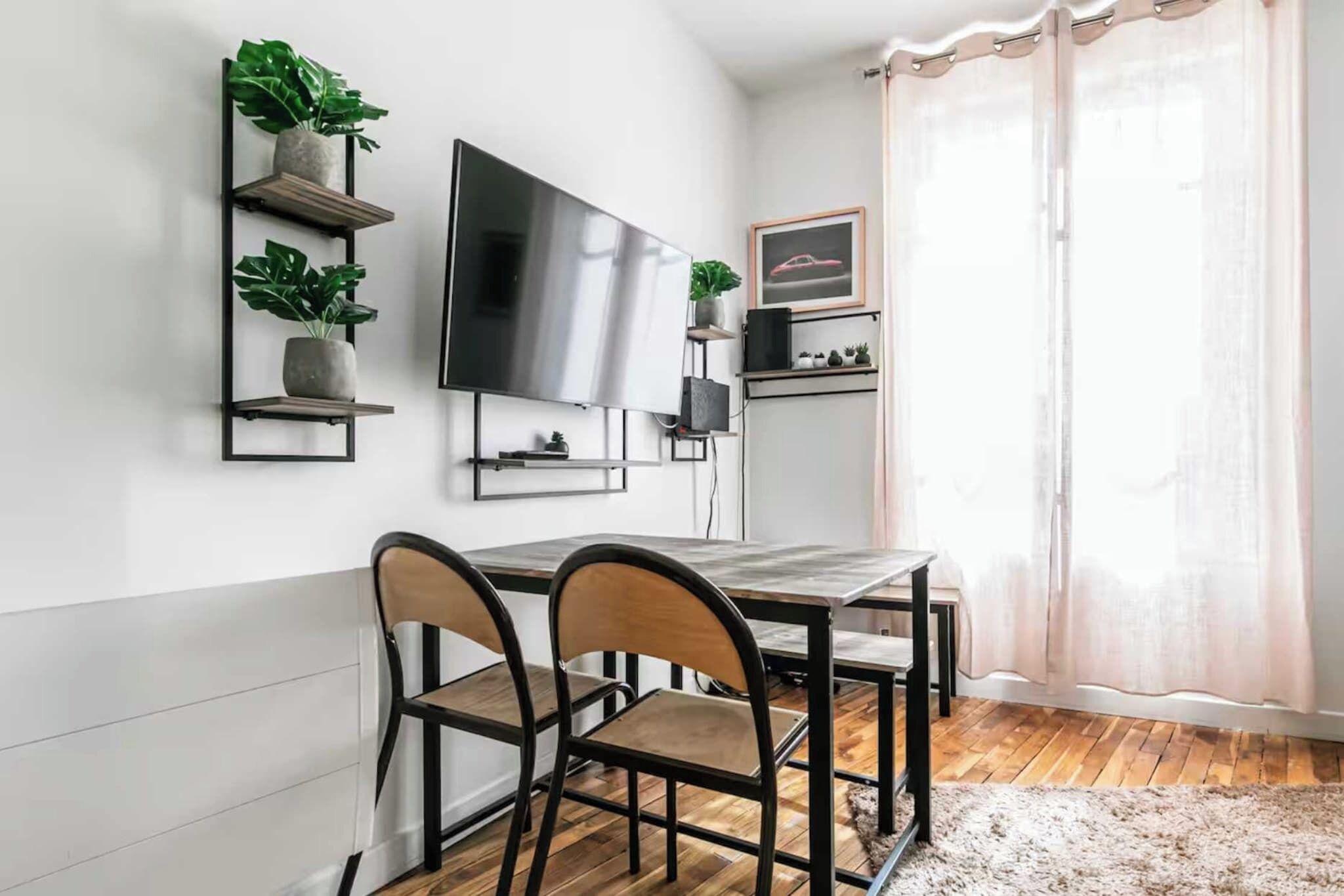 A modern dining area with a wooden table and chairs, a flat-screen TV mounted on the wall, and potted plants on shelves.