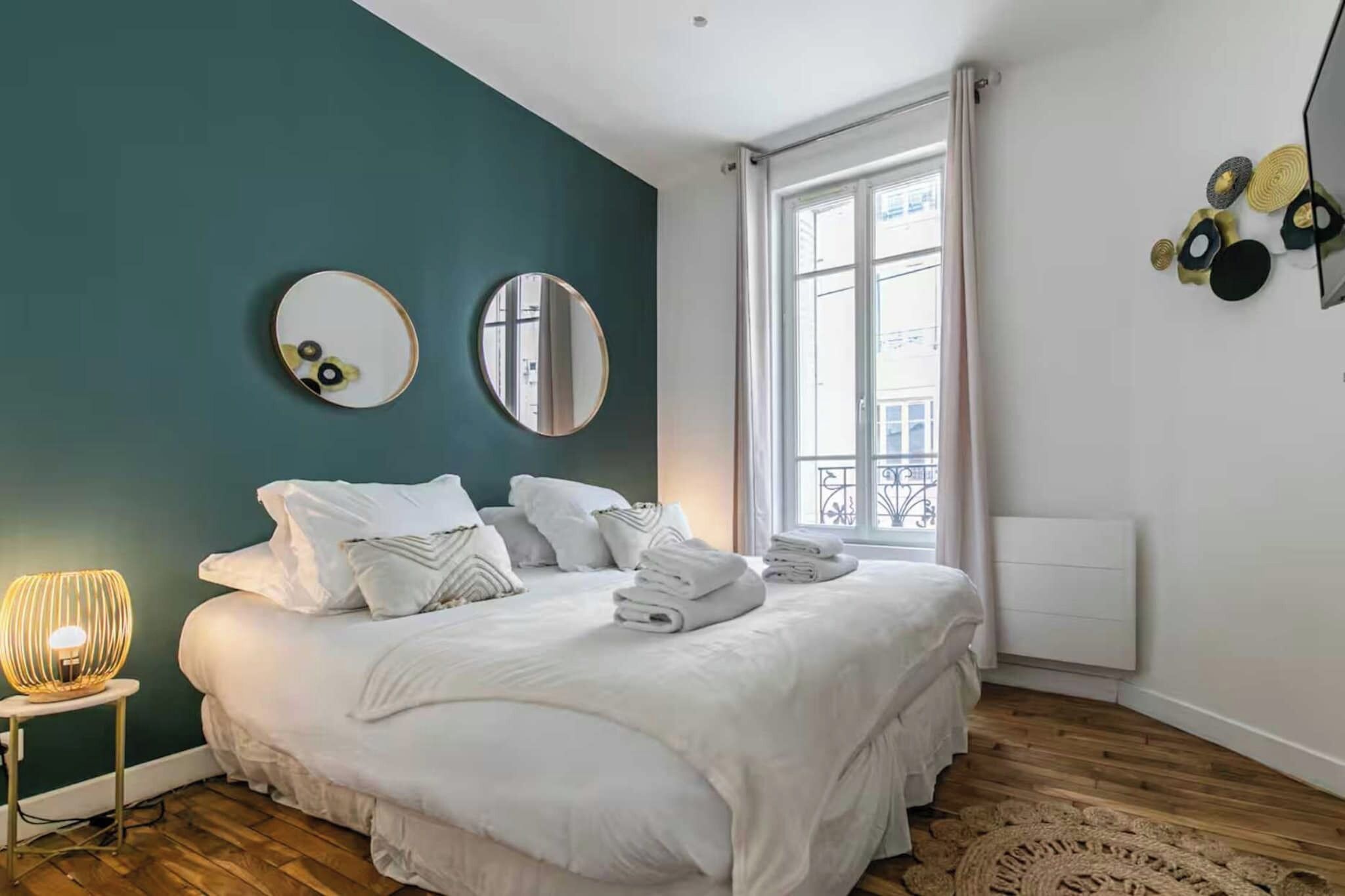 A bedroom with a bed, two round mirrors, a bedside lamp, and a window with curtains.