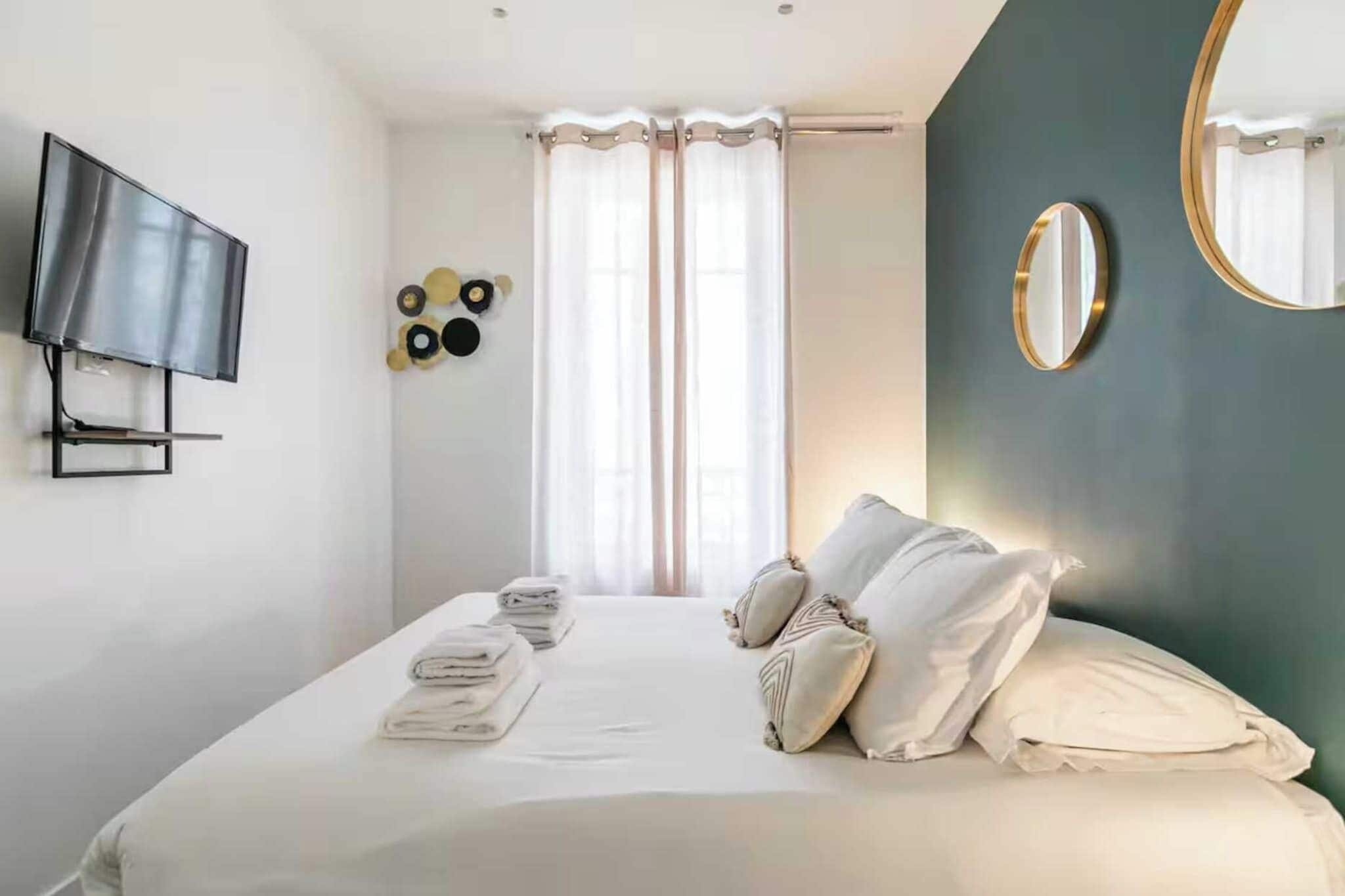 Ein Hotelzimmer mit Bett, Flachbildfernseher an der Wand, großem Spiegel und einem fenster mit Vorhängen.