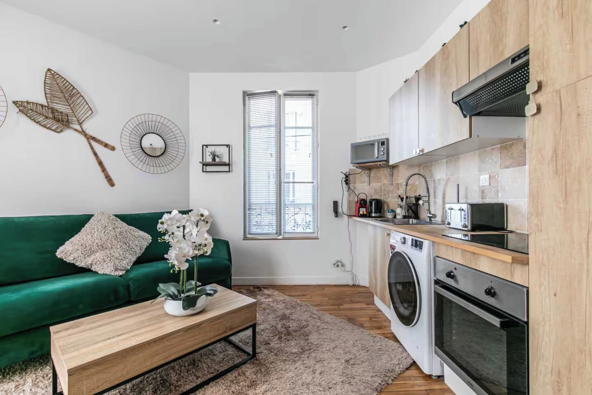 Een gezellig, ruimtelijk interieur met een groene bank, een houten salontafel, een wasmachine, een magnetron en een gootsteen.