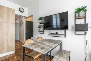 A modern living space with a dining table, chairs, a flat-screen TV mounted on the wall, and a wooden cabinet. - Charming apartment - 2BR/6P - Montreuil near Paris (Montreuil)