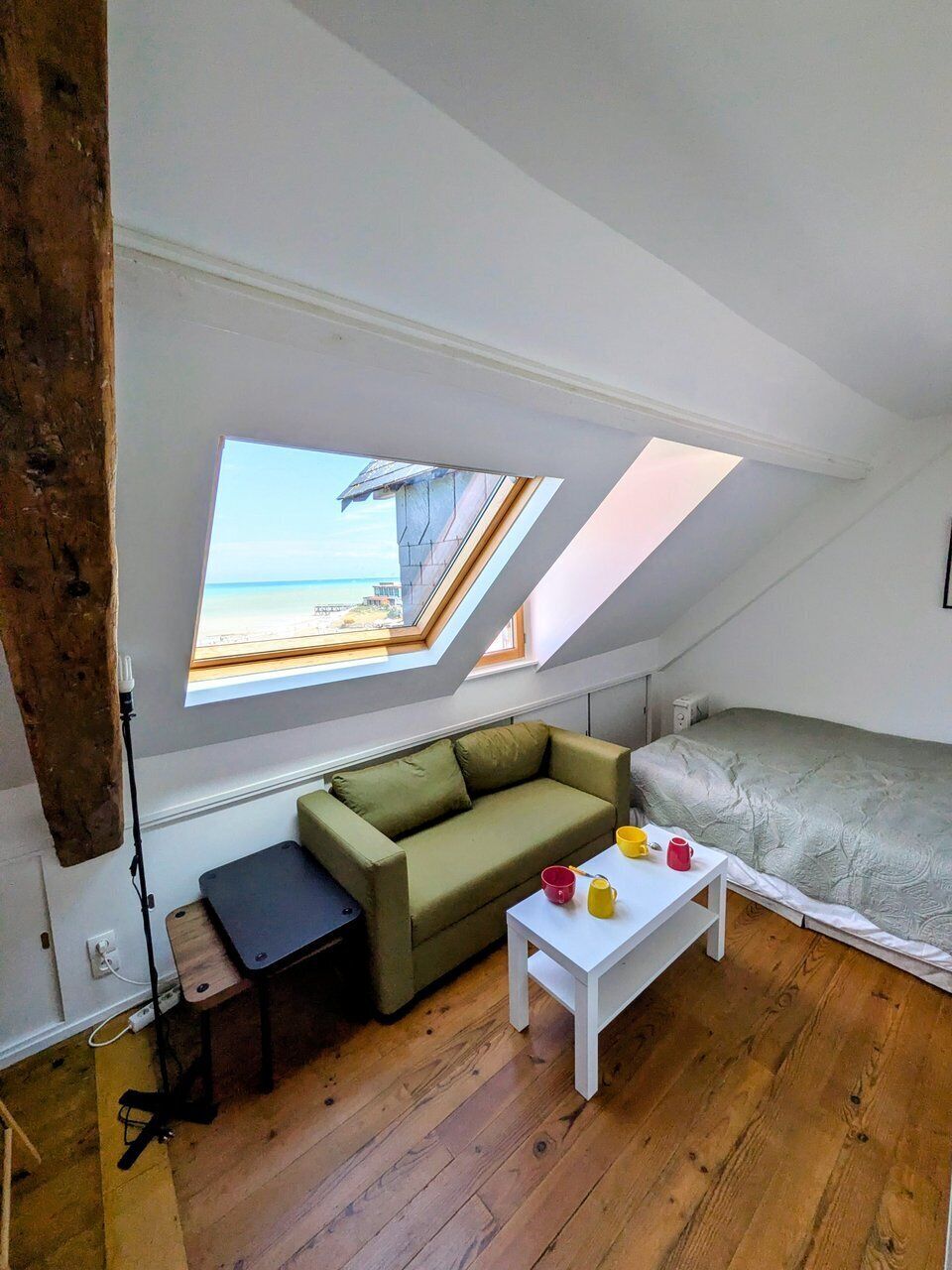 A small, cozy room with a sloped ceiling, a green sofa, a white coffee table, and a view of the beach through skylights.