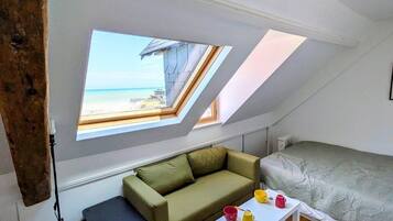 A small, cozy room with a sloped ceiling, a green sofa, a white coffee table, and a view of the beach through skylights.