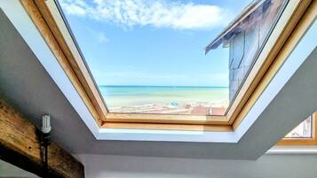 Habitación con tragaluz que da a una playa, un sofá y estructura de vigas de madera.
