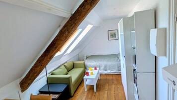 Una habitación pequeña con techo inclinado, un sofá verde, una mesita y una cama.