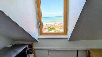 Ein kleiner Dachraum mit geneigter Decke, einem Fenster mit Blick auf den Strand und eingebauten Stauraumschränken.