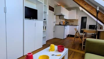 Eine kompakte Küche mit weißen Schränken, einem Esstisch mit Tassen und einer Holzbalkendecke.