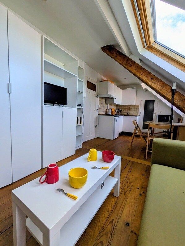 Une cuisine compacte avec des meubles blancs, une table à manger avec des tasses et un plafond avec une poutre en bois.
