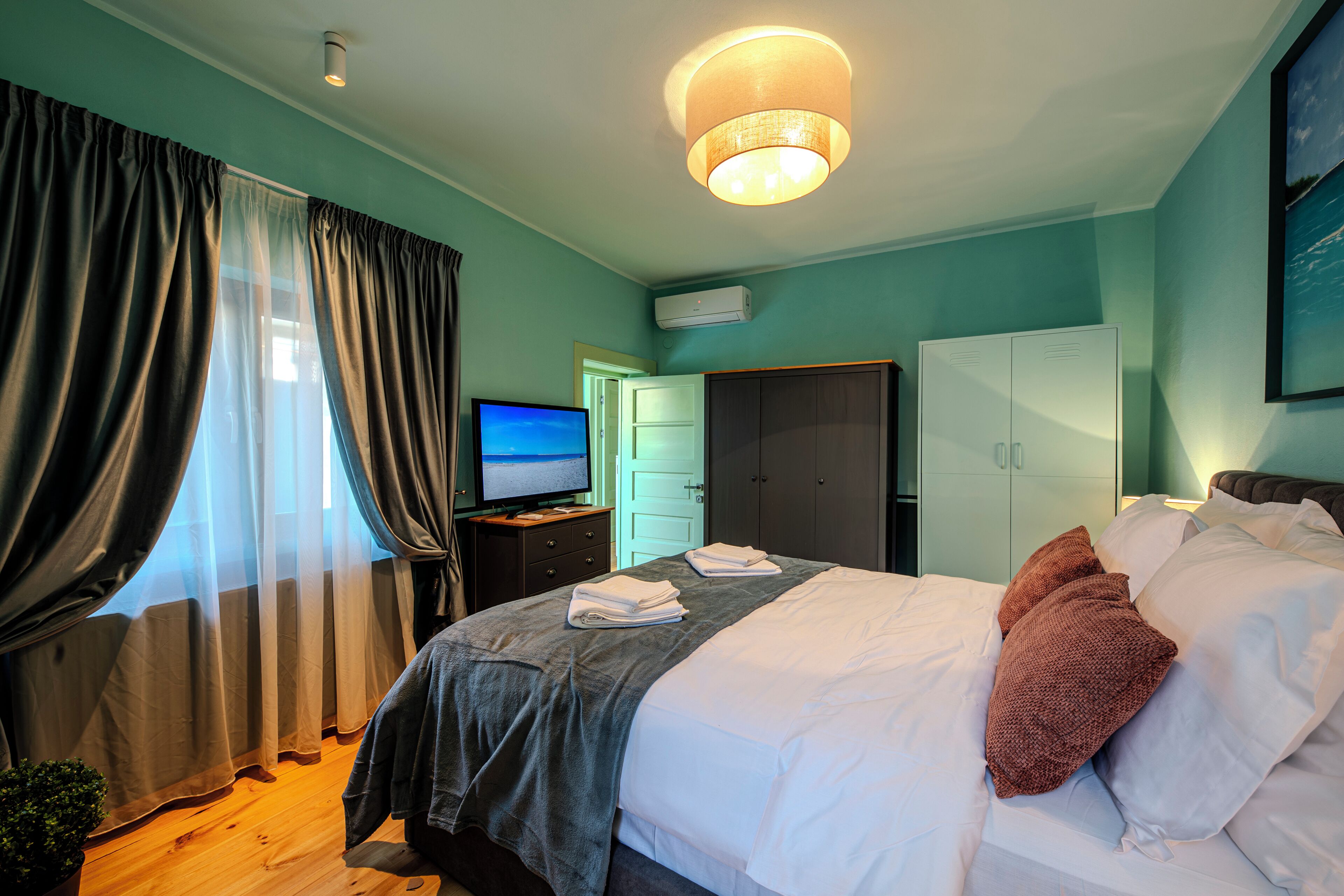 A hotel room with a bed, a television, a wardrobe, and a desk.