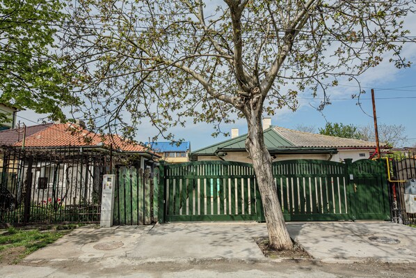 A gated residential area with a tree in the foreground, a metal fence, and a building with a tiled roof.