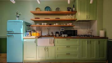 Une cuisine avec un réfrigérateur ancien, des étagères en bois et une cuisinière à gaz.