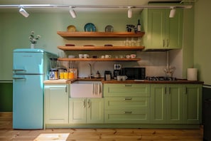Una cocina con un refrigerador antiguo, repisas de madera y una estufa a gas.
