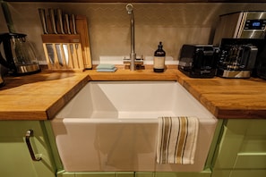 A kitchen with a sink, wooden countertop, and various appliances including a coffee maker and toaster.