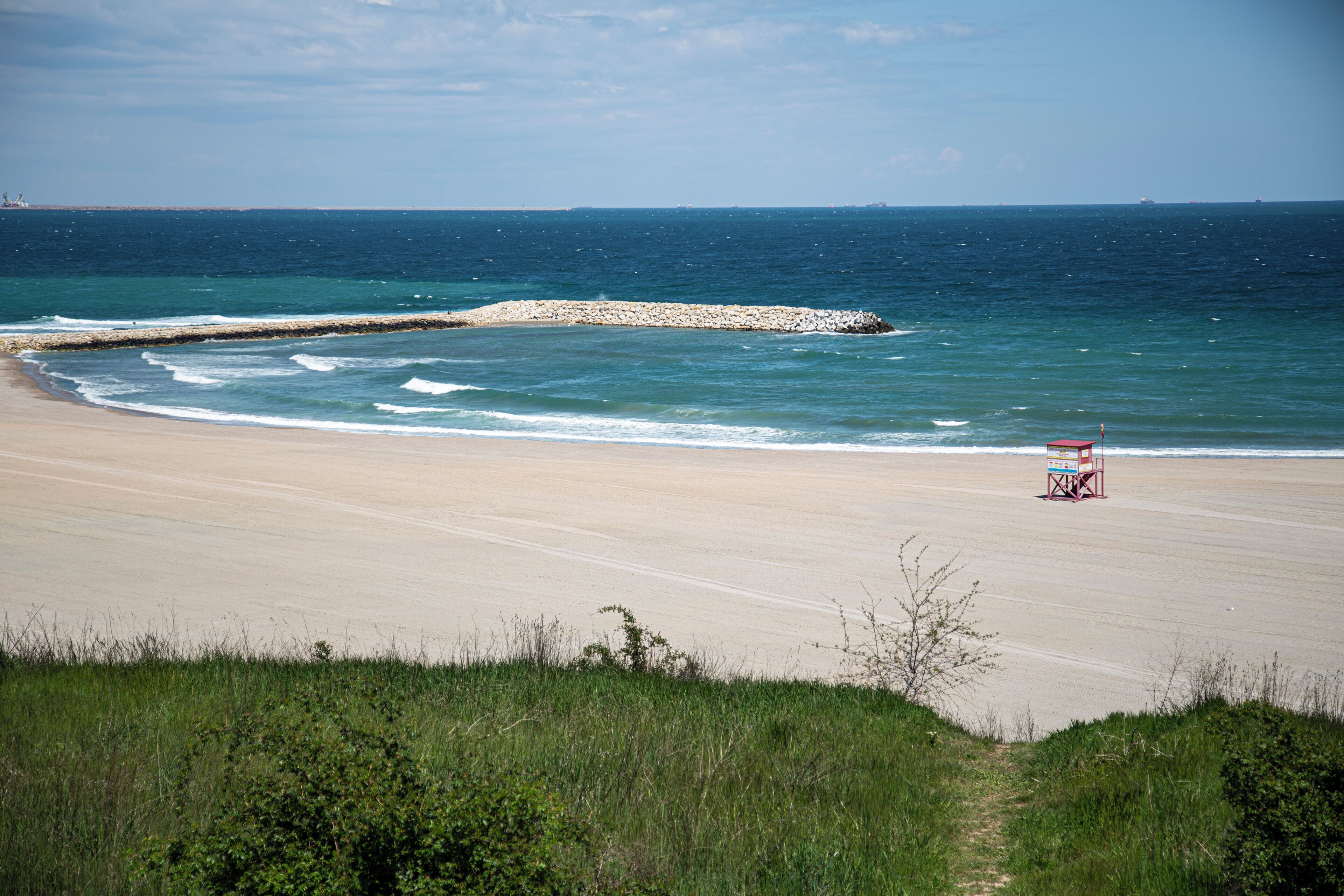A beach with a lifeguard tower, a rocky breakwater, and a clear sky.