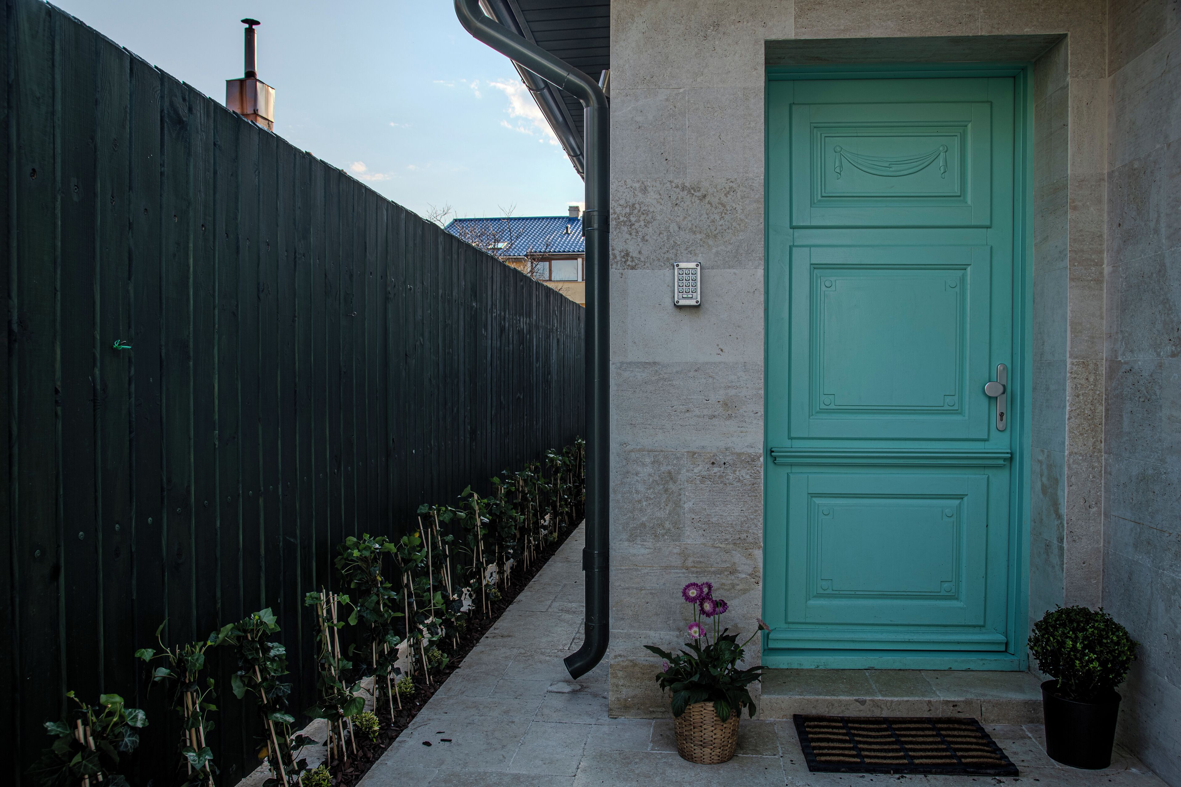 Une maison avec une porte verte, une clôture noire et un petit jardin avec des plantes et des fleurs.