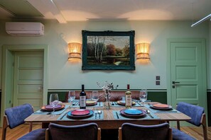 Un comedor con una mesa lista para cuatro personas, dos lámparas de pared, un cuadro enmarcado y una puerta verde.