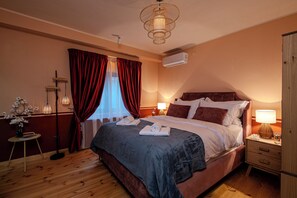 A hotel room with a bed, bedside tables, a lamp, a vase with flowers, and a window with curtains.