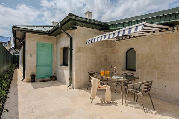 Un patio exterior con una mesa y sillas, una puerta verde y un área techada con toldo a rayas.