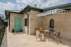 Un patio exterior con una mesa y sillas, una puerta verde y un área techada con toldo a rayas.