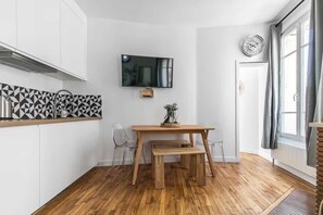 Une cuisine de taille réduite avec une table en bois, un téléviseur fixé au-dessus, et une fenêtre avec des rideaux.