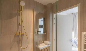 Een moderne badkamer met een goudkleurige douche, een wit wastafelmeubel en een douchecabine met glazen deuren.
