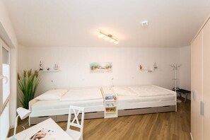 A compact room with a single bed, a small desk, and a chair. There is a bookshelf with books and a plant. - 7 in Villa Meeresblau (Cuxhaven)