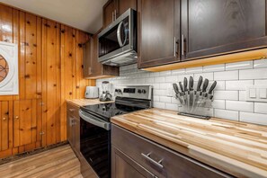 A modern kitchen with wooden cabinets, a microwave, an oven, a coffee maker, and a knife block. - Bearfoot Cabin - Central Tahoe Cabin (South Lake Tahoe)