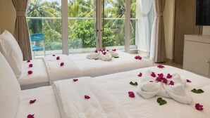 Une chambre d’hôtel avec deux lits, une grande fenêtre donnant sur des palmiers et un téléviseur fixé au mur.