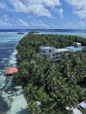 A tropical island with a resort building surrounded by dense palm trees and clear turquoise waters.