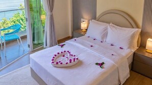 Une chambre d’hôtel avec un lit, une table de chevet, une lampe, une vue sur la mer et une chaise près de la fenêtre.