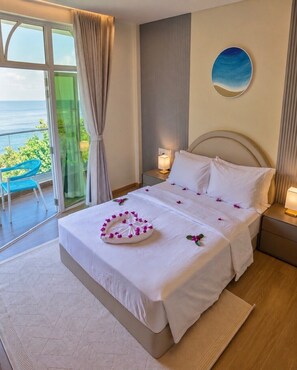 A hotel room with a bed, a nightstand, a lamp, a view of the sea, and a chair by the window. - Waterside Maldives  (Dhidhdhoo)