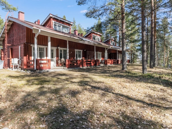 Kaksikerroksinen puinen mökki, jossa on kuisti, ja sen ympärillä on puita.