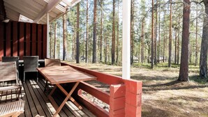 En utomhusveranda av trä med ett bord och stolar, omgiven av en skog.