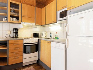 Een praktische keuken met houten kastjes, een inbouwoven, een magnetron, een koffiezetapparaat en een vaatwasser.