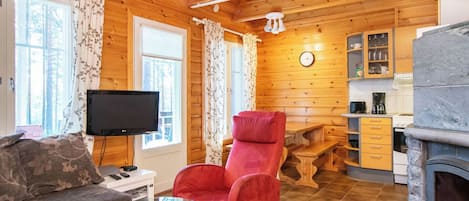 Tunnelmallinen mökin sisustus, jossa on oleskelutila, punainen nojatuoli, televisio ja kivinen takka.