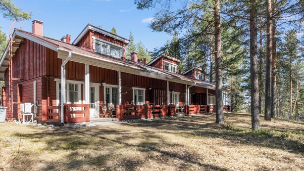 Eine zweigeschossige Holzhütte mit Veranda, umgeben von Bäumen.