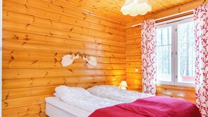 Ein Zimmer einer Holzhütte mit einem Bett, einem fenster mit Vorhängen und einer Pendelleuchte.
