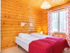 A wooden cabin room with a bed, a window with curtains, and a hanging light fixture. - Koli country club b 6 by Interhome (Lieksa)