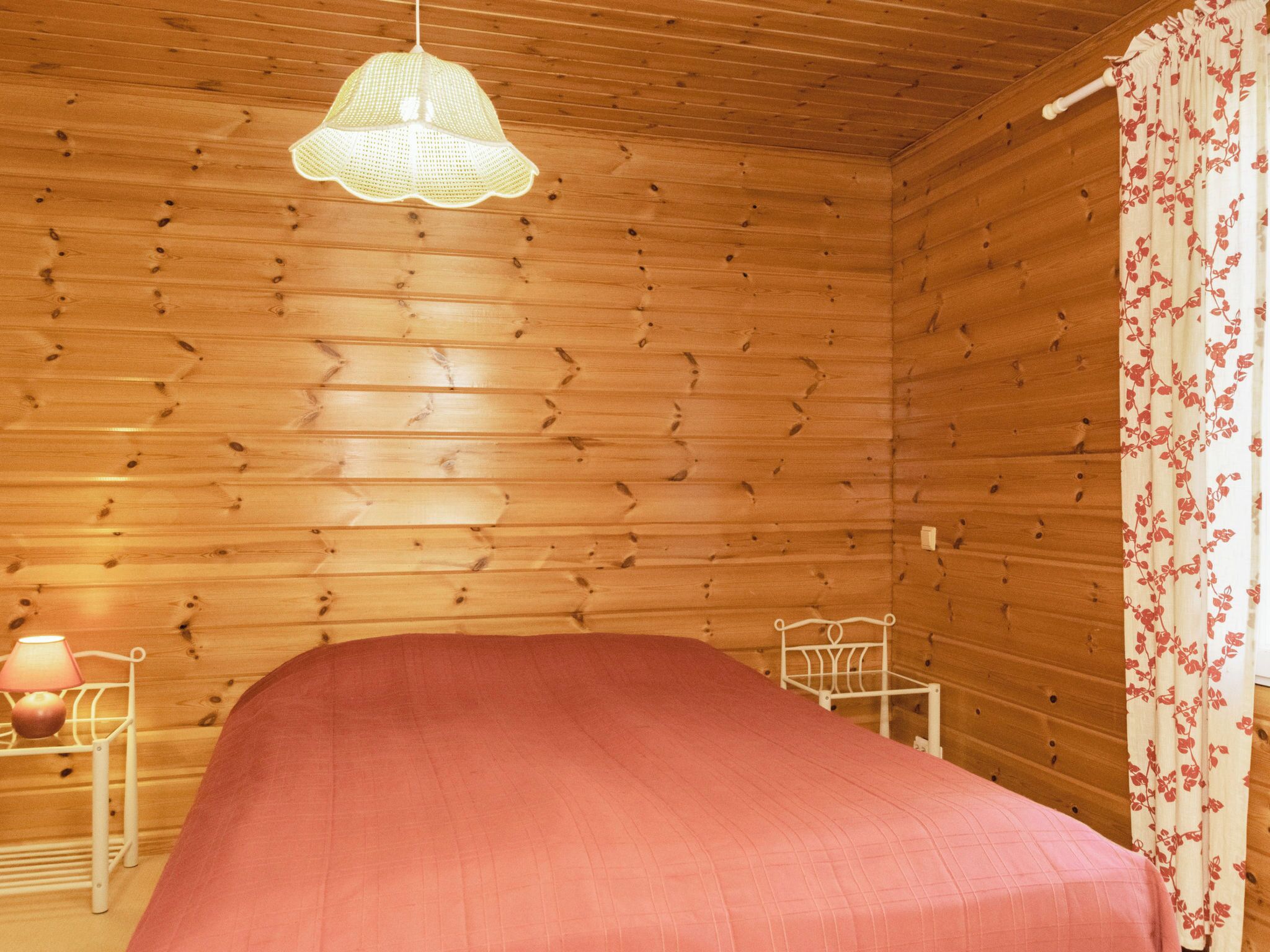 Ein Zimmer in einer Holzhütte mit einem Bett, einer Hängeleuchte, einem Sessel und einem Nachttisch mit Lampe.