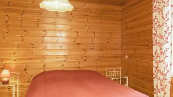 Ein Zimmer in einer Holzhütte mit einem Bett, einer Hängeleuchte, einem Sessel und einem Nachttisch mit Lampe.