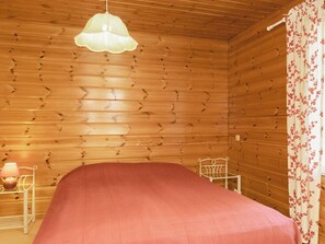 A wooden cabin room with a bed, a hanging light fixture, a chair, and a nightstand with a lamp. - Koli country club b 7 by Interhome (Lieksa)