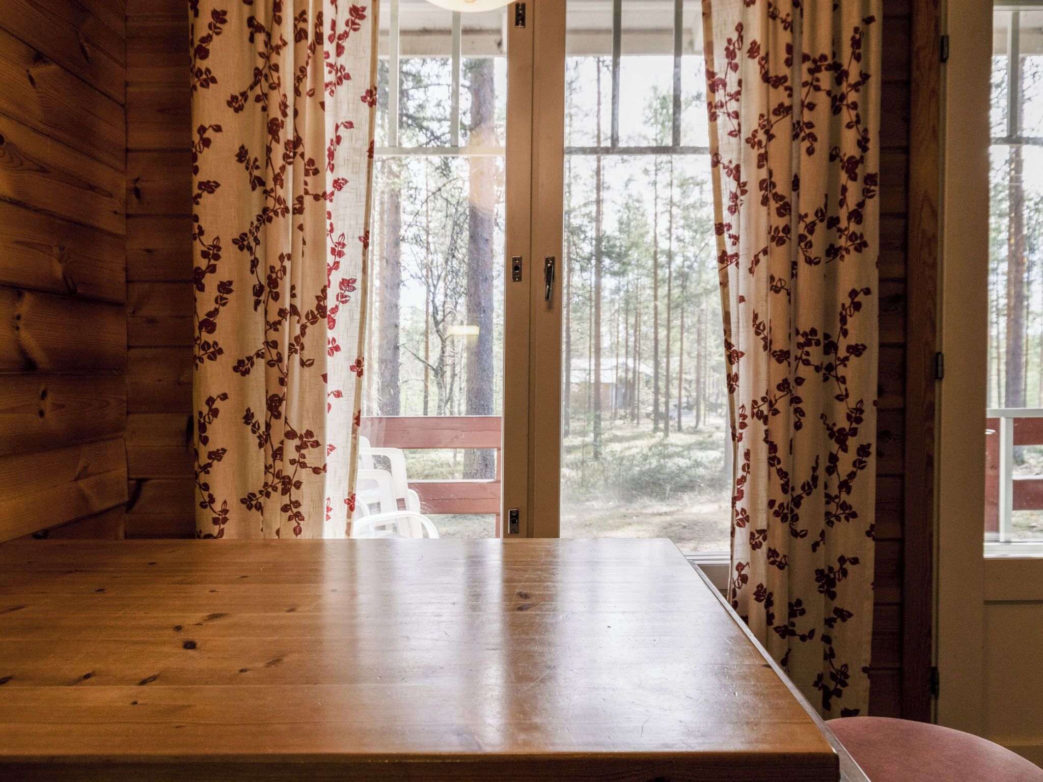 Ein Holztisch in einem Zimmer mit Blick auf einen Wald durch eine Glastür.