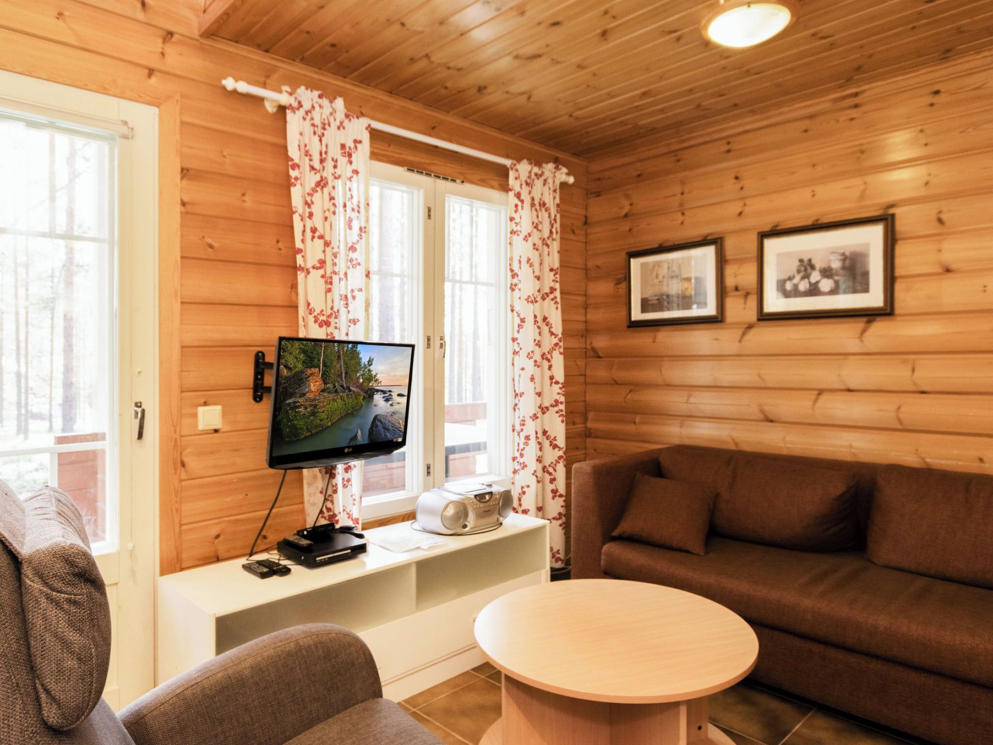 Een knus interieur met een televisie op een standaard, een bank, een ronde tafel en een raam met gordijnen.