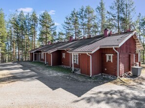 Een rij rode houten bungalows met een grindpad en een bebost landschap op de achtergrond.