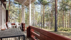 Et overdækket udendørs siddeområde med bord og stole, omgivet af en træterrasse og skov.