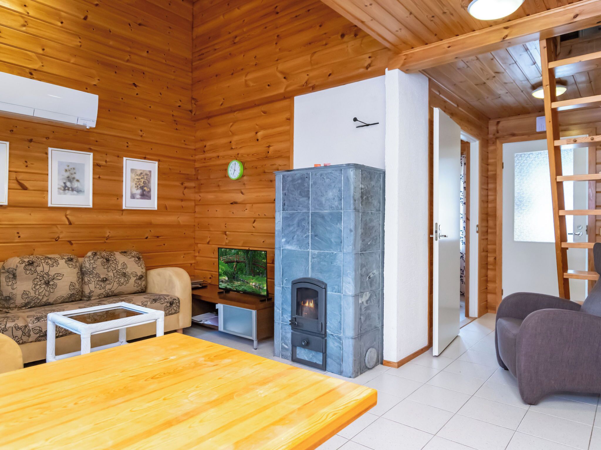 L’intérieur chaleureux d’un chalet avec un canapé, une table en bois, un téléviseur et une cheminée en pierre.