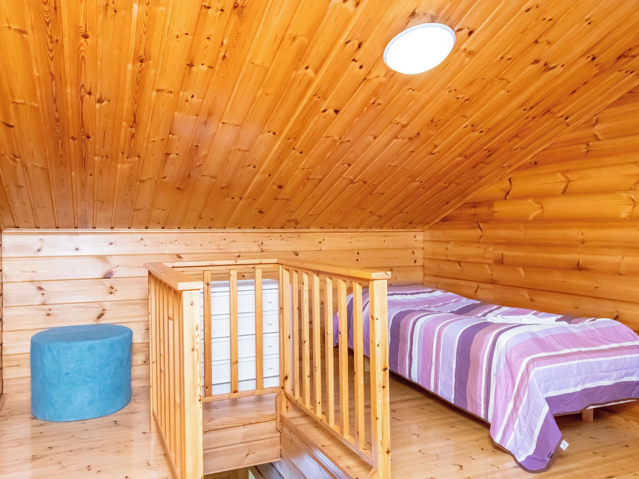 Une pièce dans une cabane en bois, avec un lit superposé, un petit tabouret bleu et un berceau en bois.